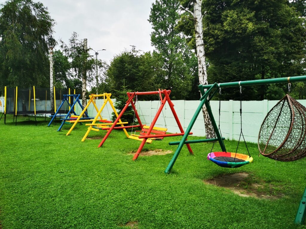 zdjęcie przedstawia fragment ogrodu z trampoliną, huśtawkami ogrodowymi oraz huśtawkami dla dzieci. 