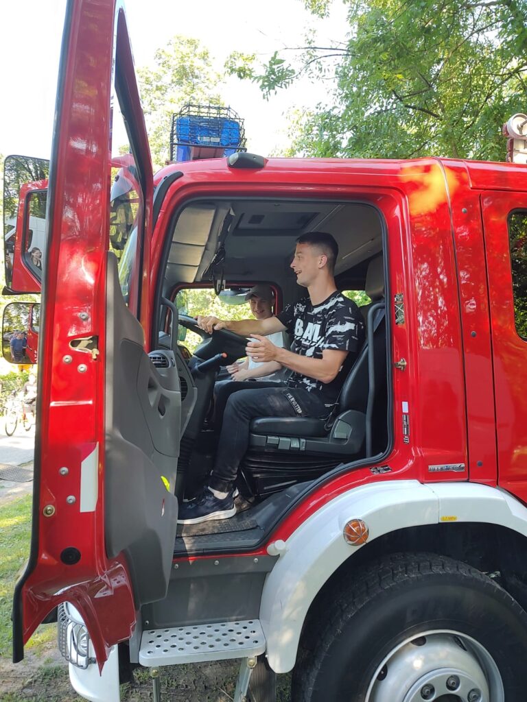 Chłopak siedzi za kierownicą wozu strażackiego. 