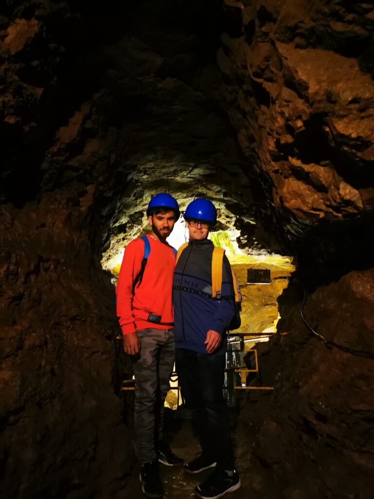 Dwoje chłopców w kaskach stoi przy ścianie w podziemiu kopalni. 
