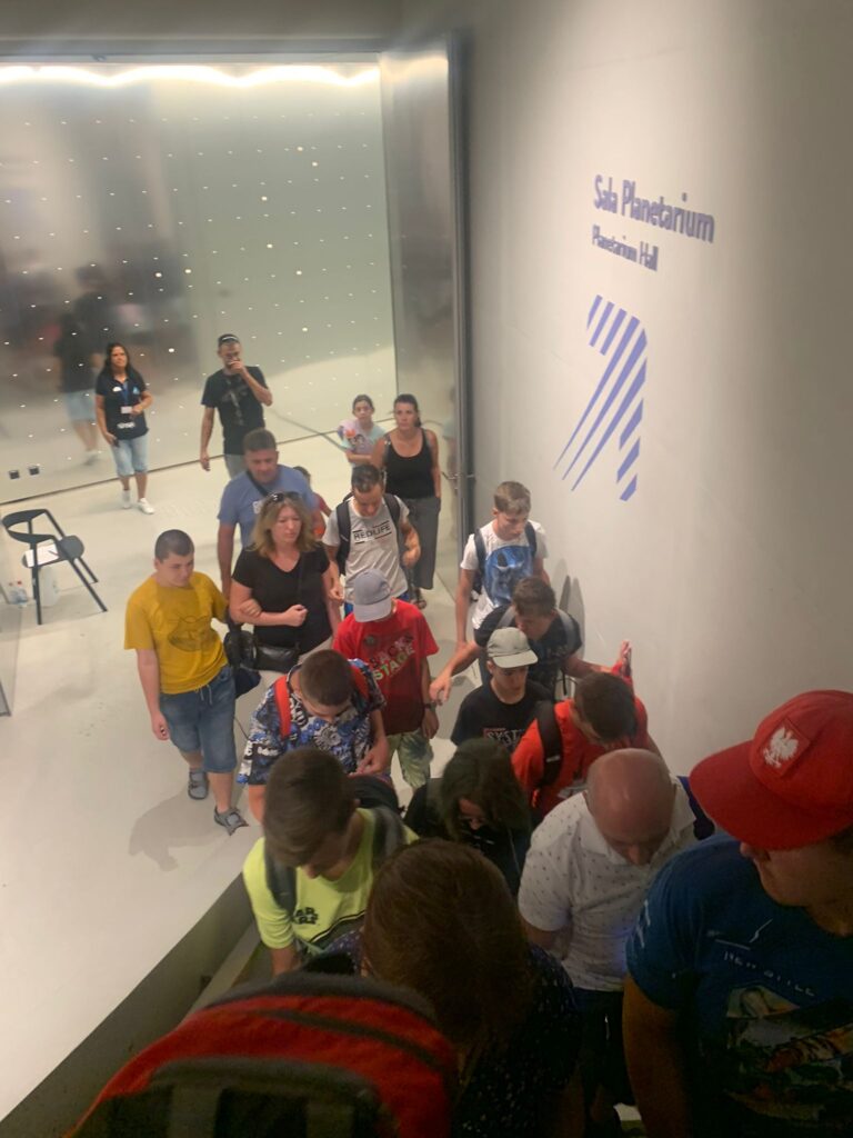 Grupa osób wchodzi po schodach. Na ścianie napis "Sala Planetarium"
