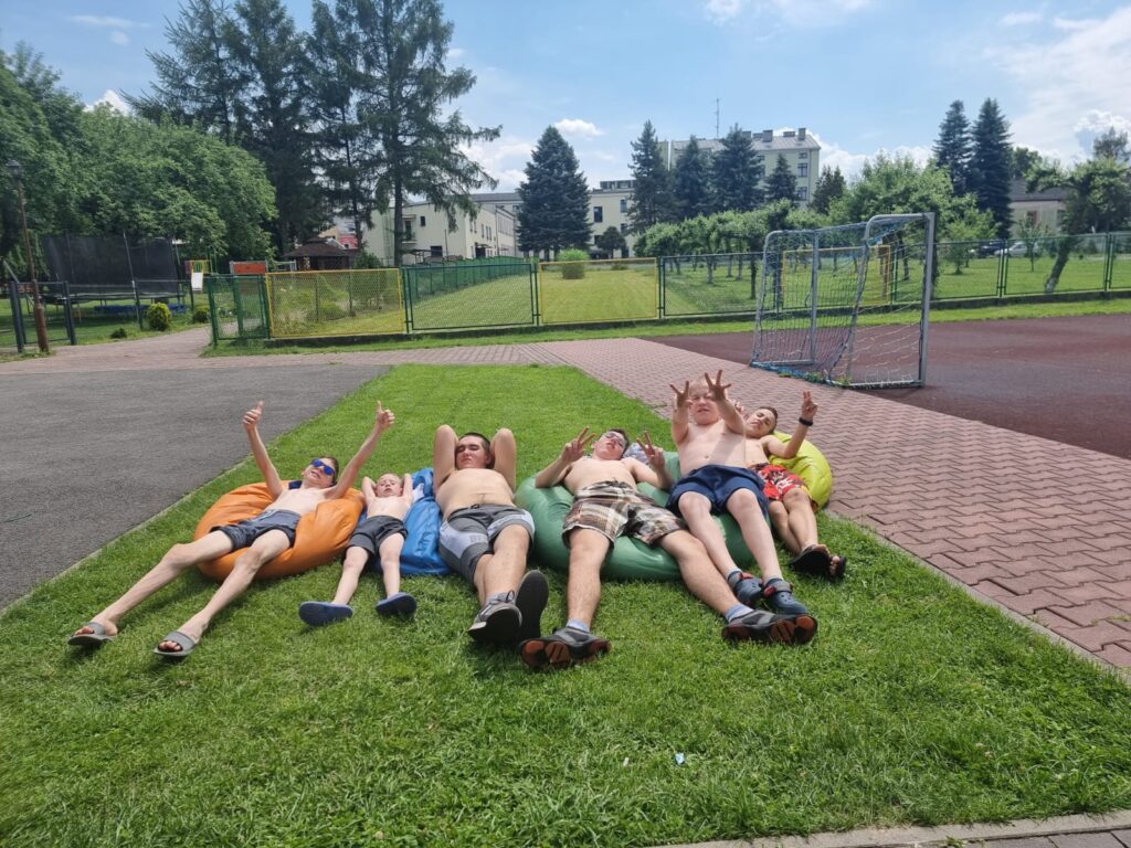 grupa chłopaków w różnym wieku leży na trawie i się opala. 