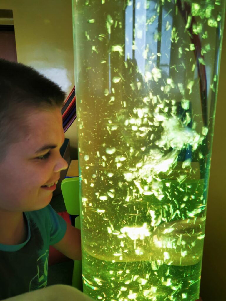 chłopiec przyglądający się podświetlonej przezroczystej tubie, w której znajduje się woda i wirują bąbelki 