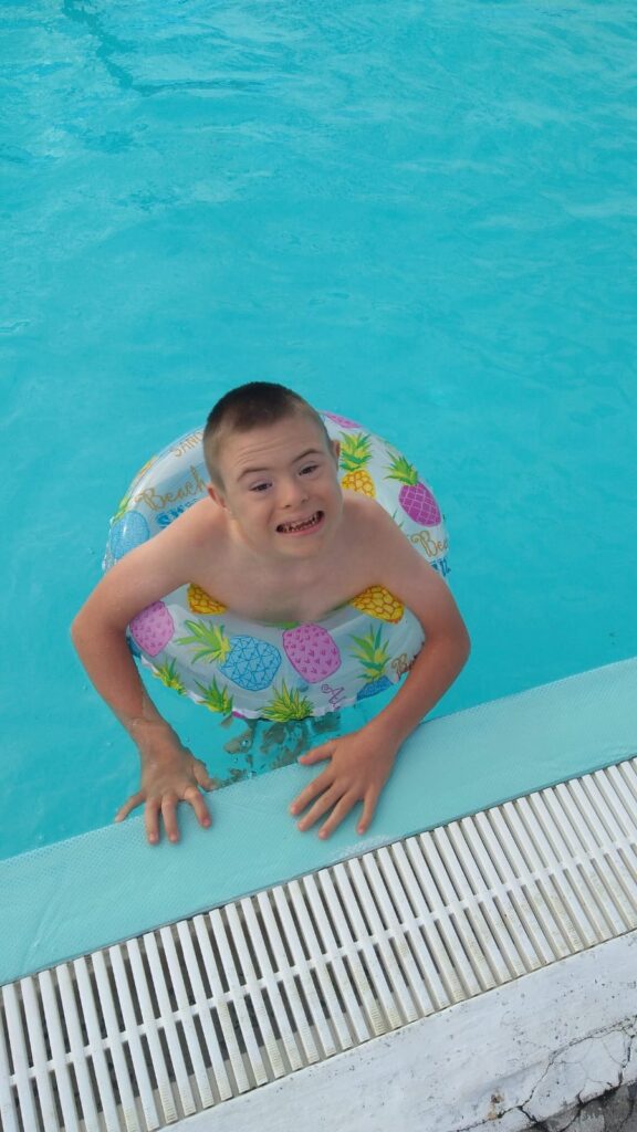 Chłopiec z zespołem Downa pływa w basenie z pomocą dmuchanego koła 