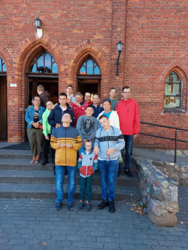Grupa osób przed wejściem do ceglanego kościoła 