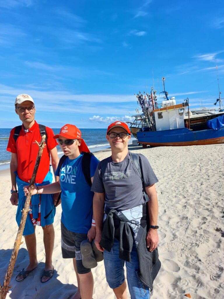 Troje Panów na plaży pozujących przed kutrem rybackim 