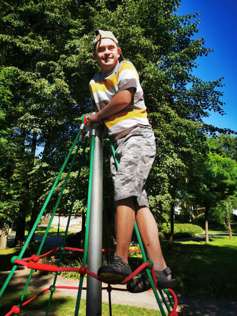 chłopak uśmiecha się stojąc na szczycie konstrukcji do wspinaczki na placu zabaw. 