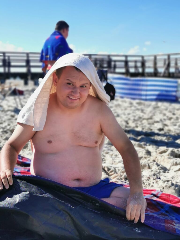 mężczyzna siedzący na plaży, na głowie ma ręcznik.