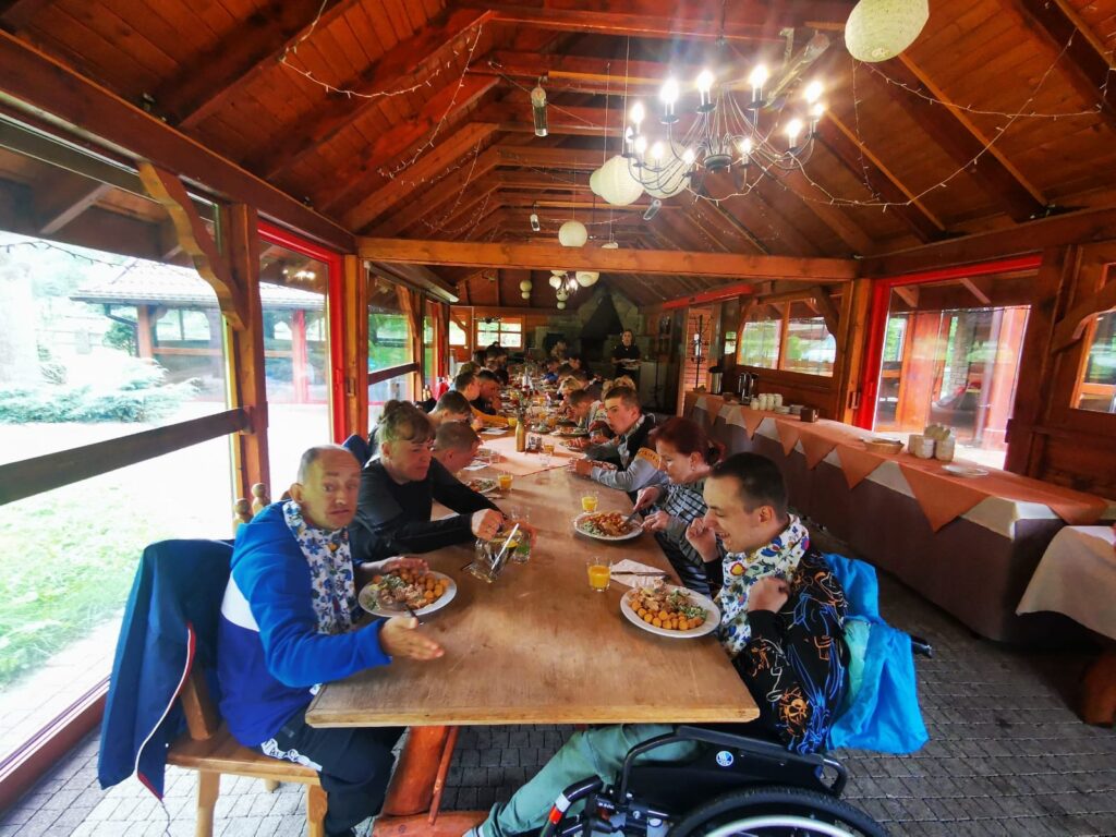 Grupa osób jedząca obiad w dużej drewnianej altanie 