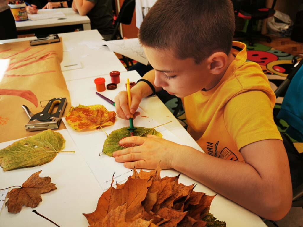 Chłopiec przy stole malujący liście. 
