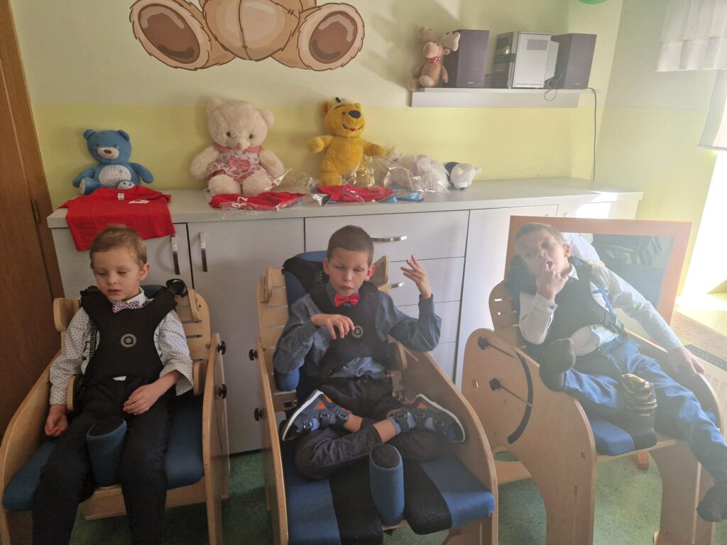 Troje chłopaków ubranych w koszula i muszki siedzących w drewnianych fotelikach dla dzieci