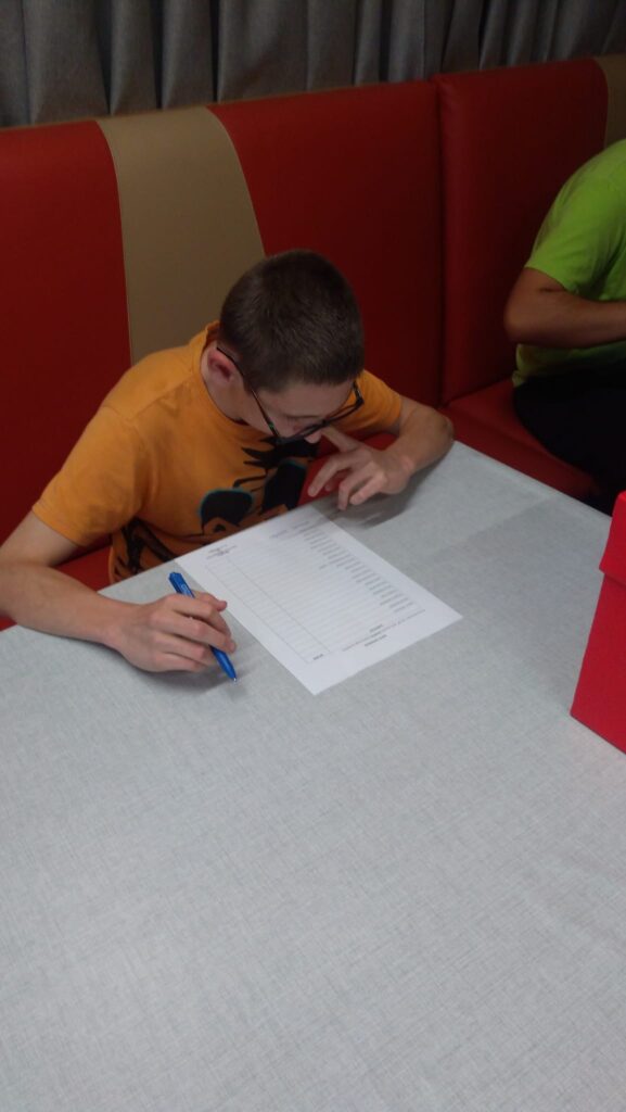 chłopiec siedzi z kartką papieru, w ręce trzyma długopis. 