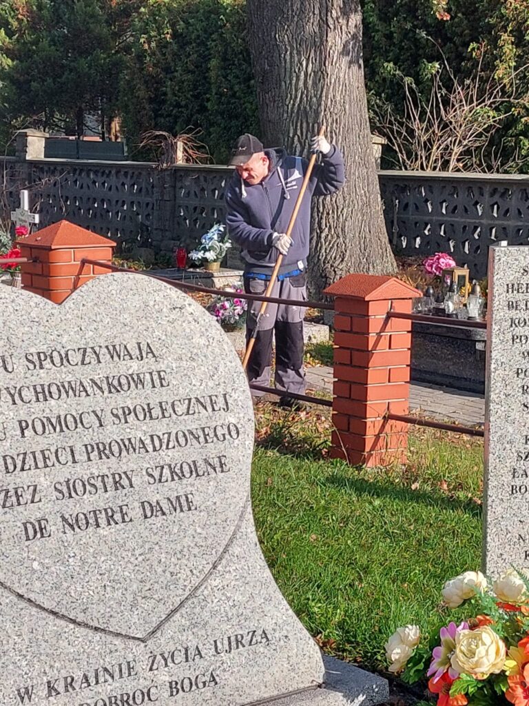 mężczyzna w stroju roboczym na cmentarzu grabi liście. 