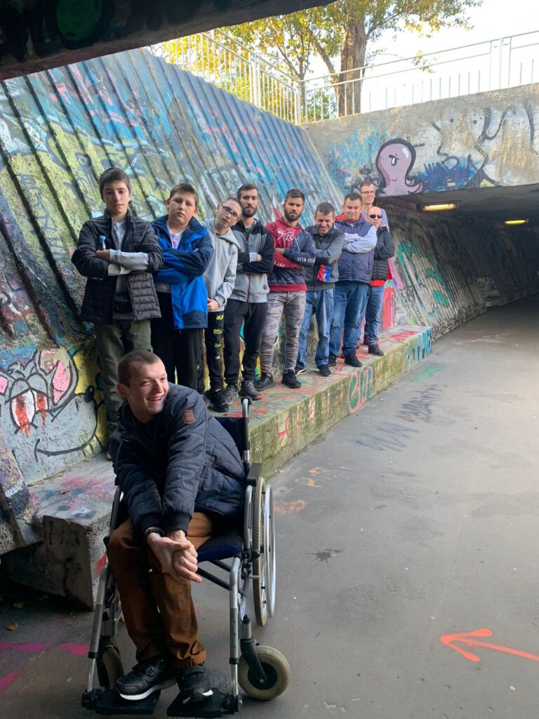 grupa mężczyzn i chłopaków pozujących pod murem z graffiti. 