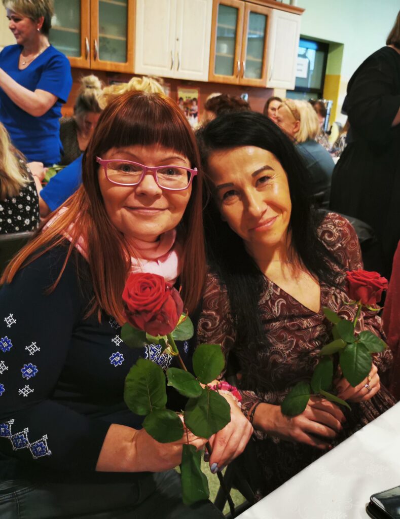 Dwie kobiety siedzą obok siebie. W rękach trzymają róże 