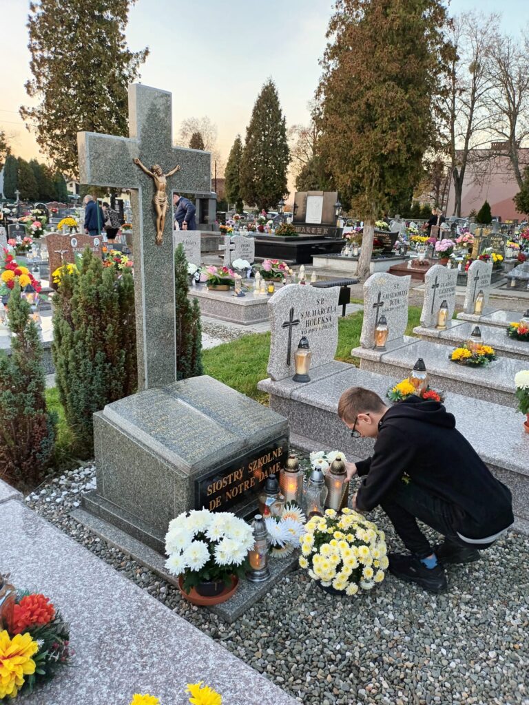 chłopiec kładzie znicz na pomniku cmentarnym podpisanym "Siostry Szkolne de Notre Dame" 