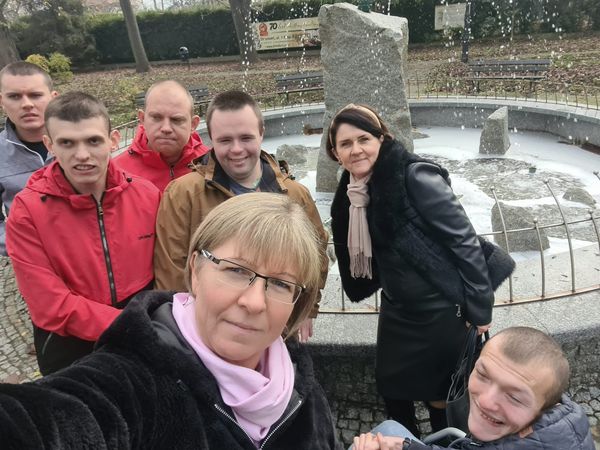 Grupa osób pozuje do zdjęcia typu selfie. ZA nimi fontanna 