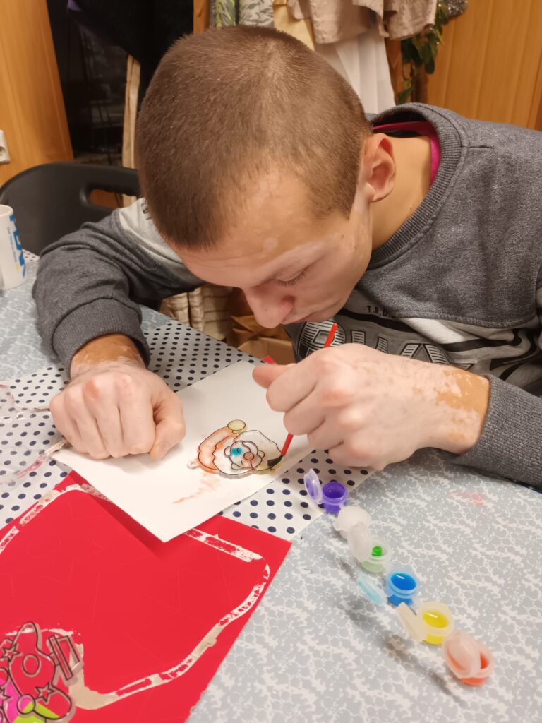 Chłopiec siedzący przy stole malujący farbkami. 