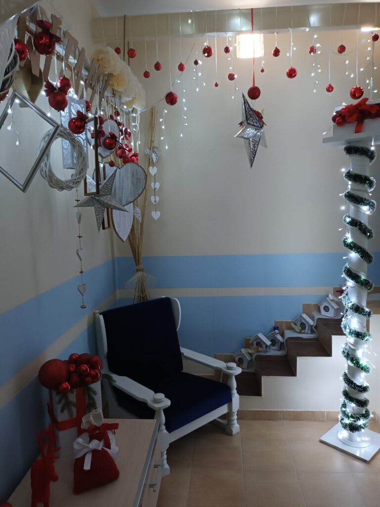 Świąteczna dekoracja: Pomieszczenie całe udekorowane - fotel, stroiki, zawieszone pod sufitem ozdoby. 