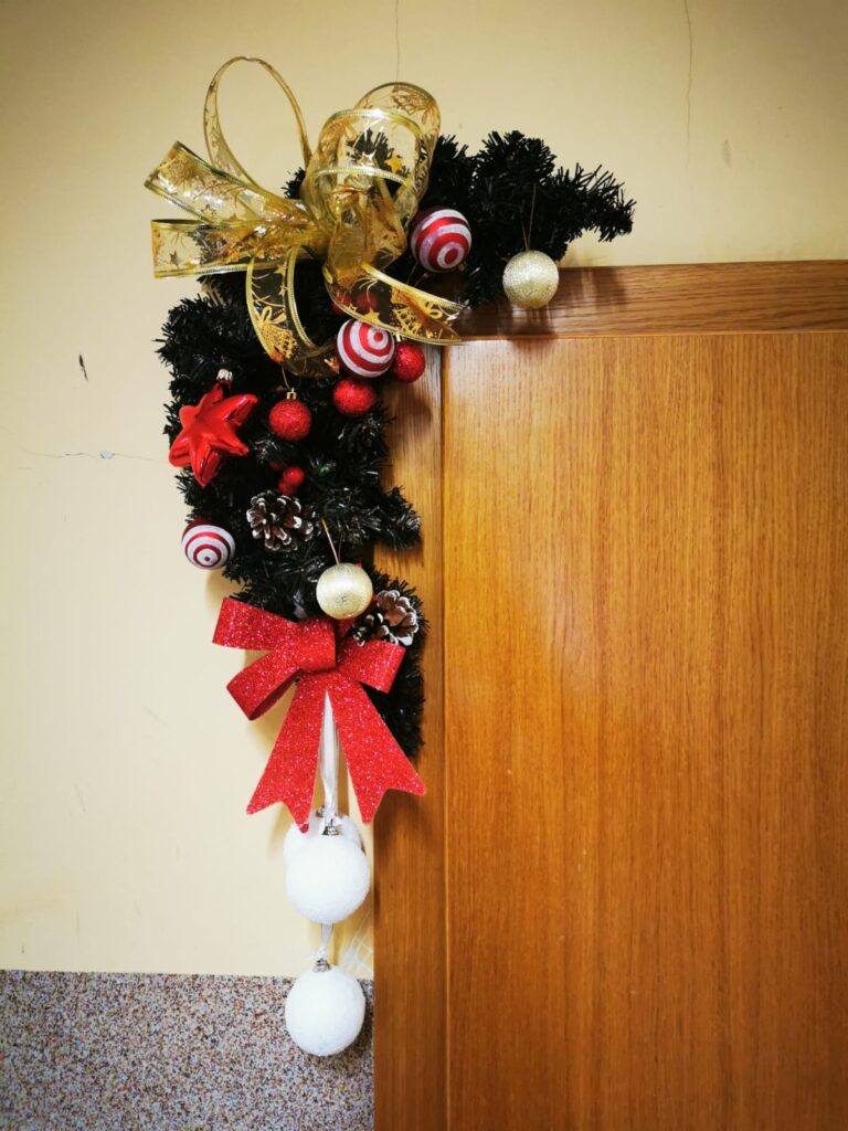 Świąteczna dekoracja: Stroik z gałęzi, bombek i wstążek zawieszony na drzwiach. 