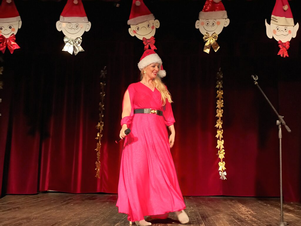 Uśmiechnięta kobieta w czerwonej sukience stoi na scenie. 