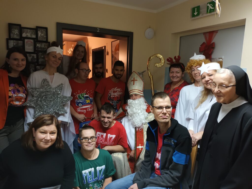Zdjęcie grupowe osób w ubraniach z motywami świątecznymi pozujących z Mikołajem. 