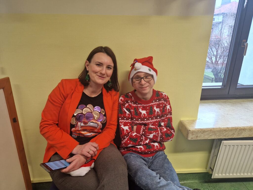 Kobieta i chłopiec w ubraniu z motywami świątecznymi siedzą i uśmiechają się do obiektywu. 