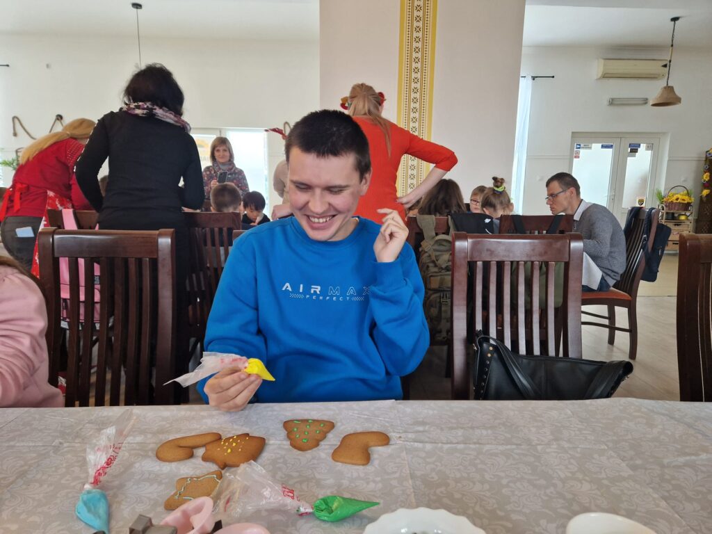 Uśmiechnięty chłopak przy stole dekoruje pierniczki. 