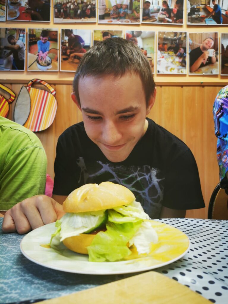 chłopiec z uśmiechem wpatrujący się w stojącego przed nim burgera. 