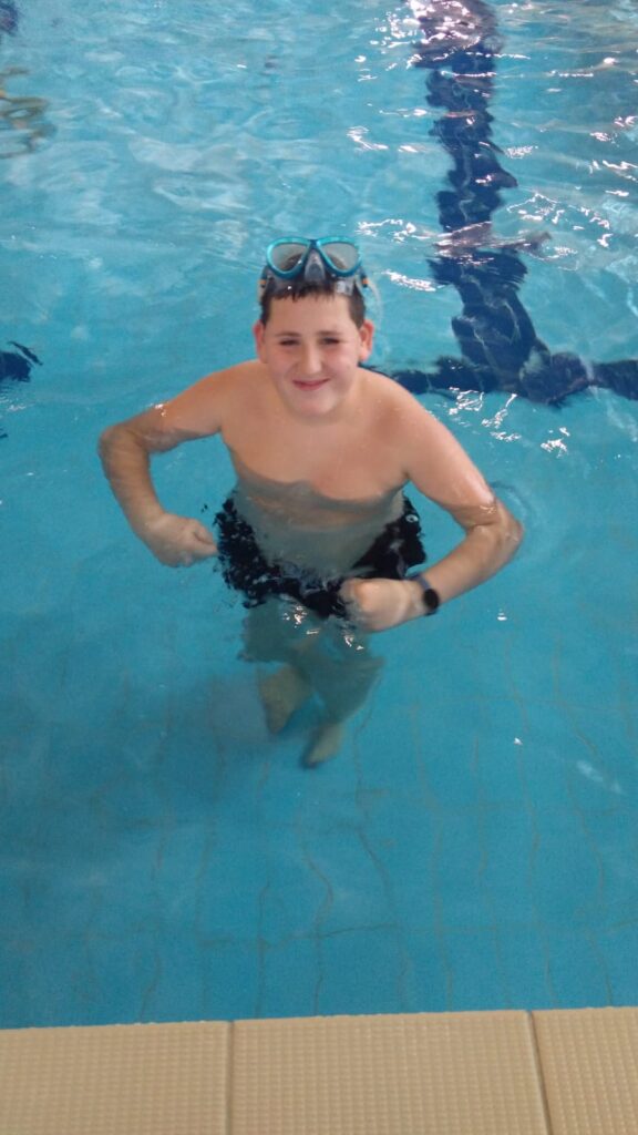 uśmiechnięty chłopiec stoi w basenie 