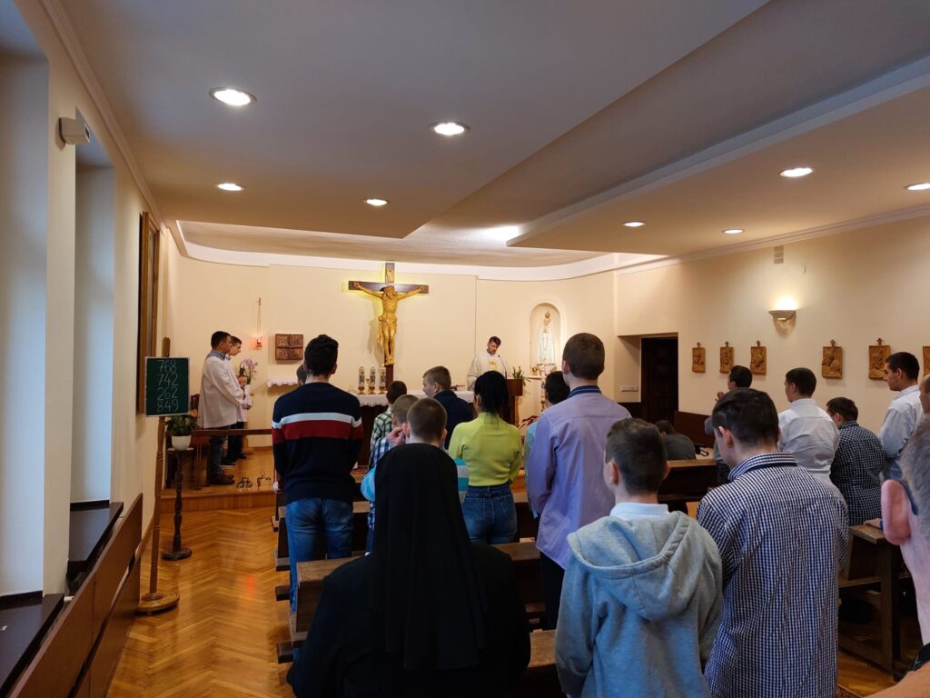 Grupa osób stojąca w kaplicy. W oddali widać duży wiszący krzyż. 