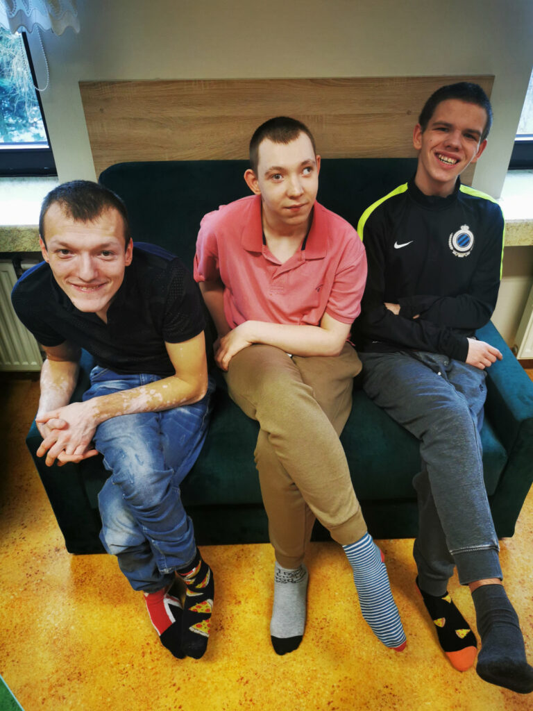 Trzech uśmiechniętych chłopaków siedzących na kanapie w kolorowych skarpetach.