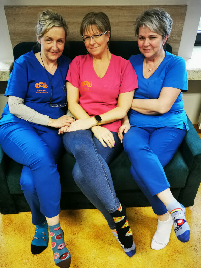 Trzy uśmiechnięte kobiety siedzące na kanapie w kolorowych skarpetach.