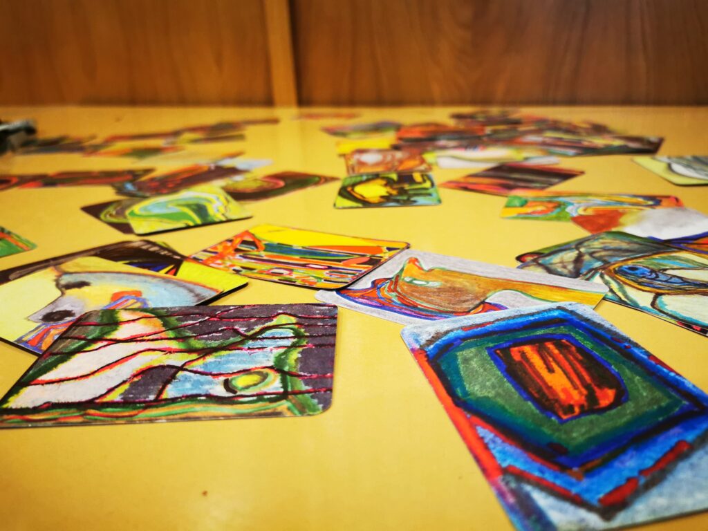 Liczne kolorowe karty z abstrakcyjnymi wzorami rozłożone na stole. 