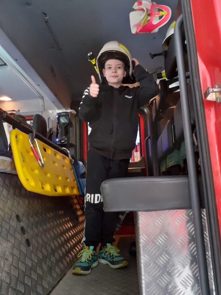Chłopiec w kasku strażaka wewnątrz wozu strażackiego. 