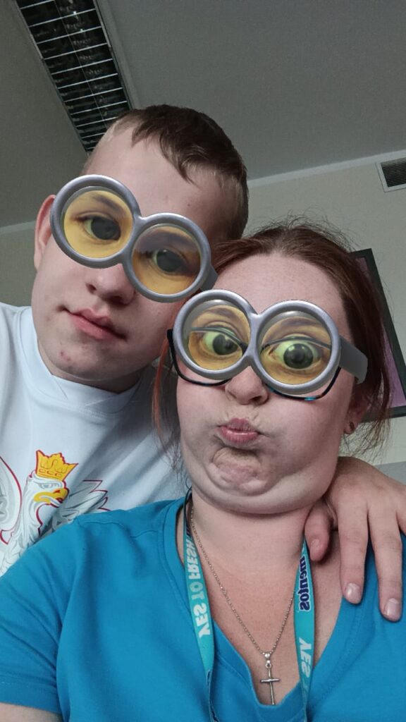 Kobieta i chłopak pozują do zdjęcia z filtrem nakładającym na ich oczy duże, powiększające oczy okulary. Kobieta dodatkowo robi dziwną minę. 