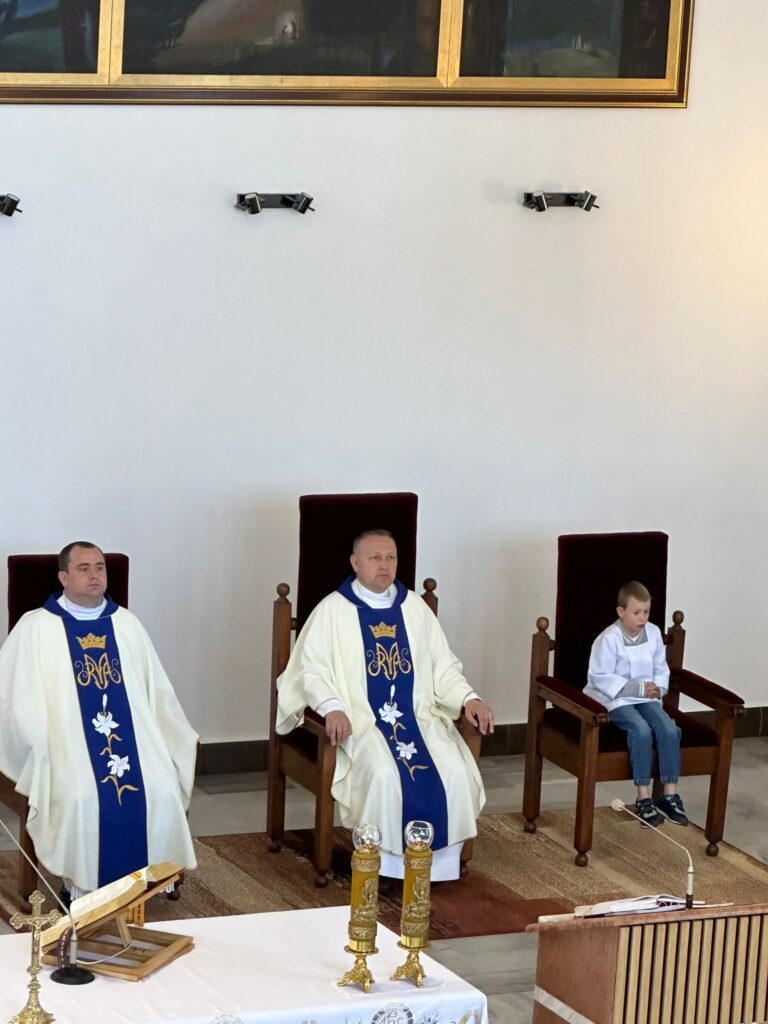 Dwóch księży i mały chłopiec siedzący w fotelach obok ołtarza. 