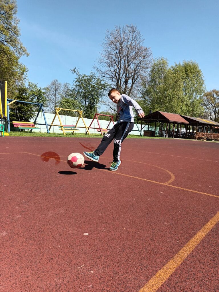 Chłopiec kopiący piłkę na boisku. 