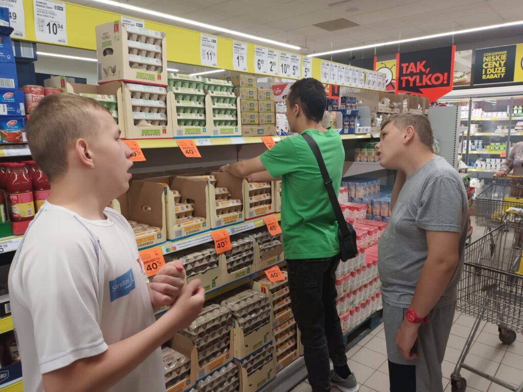 chłopaki podczas zakupów w markecie., Jeden z nich bierze z półki paczkę jajek 