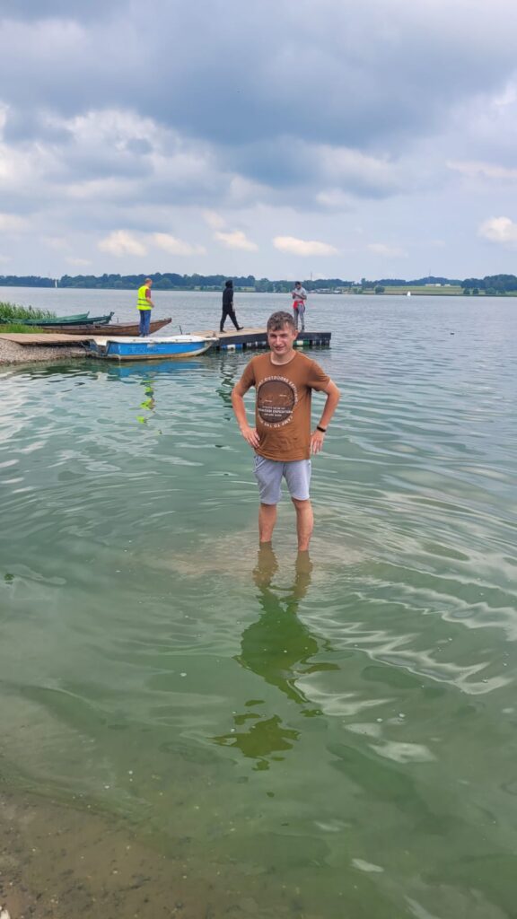 Chłopiec stojący w po kolana w wodzie jeziora. 