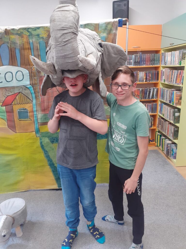 dwaj chłopców pozujący do zdjęcia. Jeden z nich ma na głowie dużą maskę słonia. 