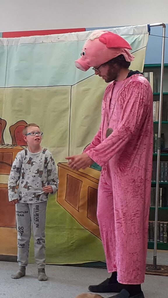 Mały chłopiec rozmawiający na scenie z mężczyzną w kostiumie świni. 
