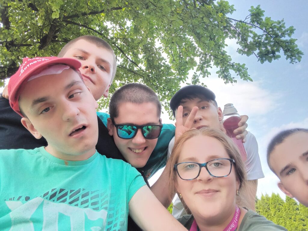 Zdjęcie grupowe typu selfie kobiety i 5 chłopaków. Za nimi niebo i drzewa. 