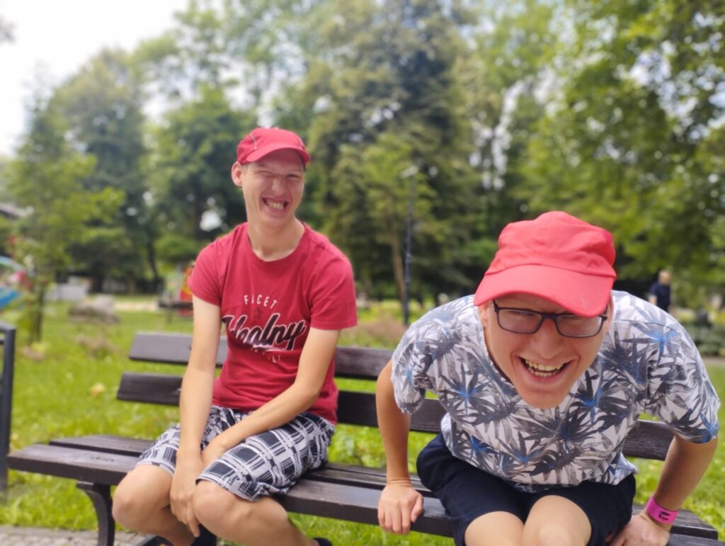Dwóch roześmianych chłopaków siedzących na ławce w parku. 
