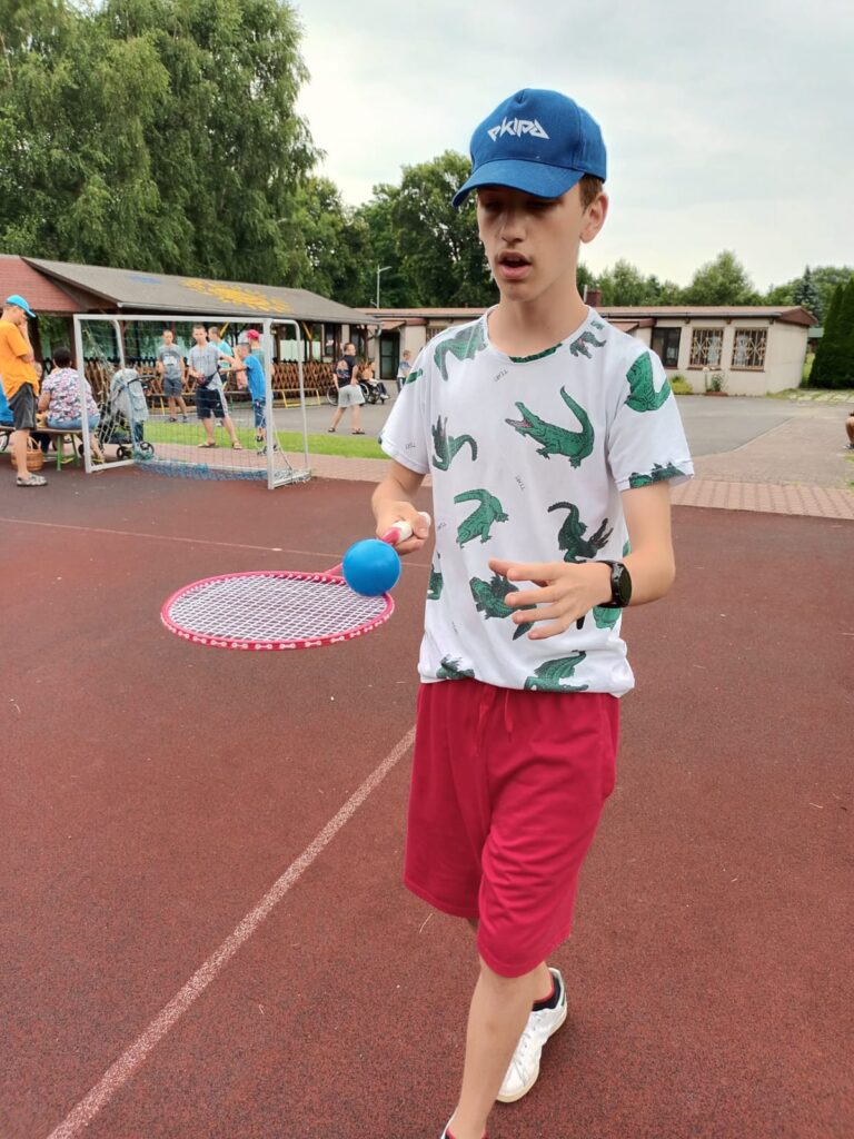 Chłopiec idący po boisku z piłeczką niesioną na paletce do badmintona 