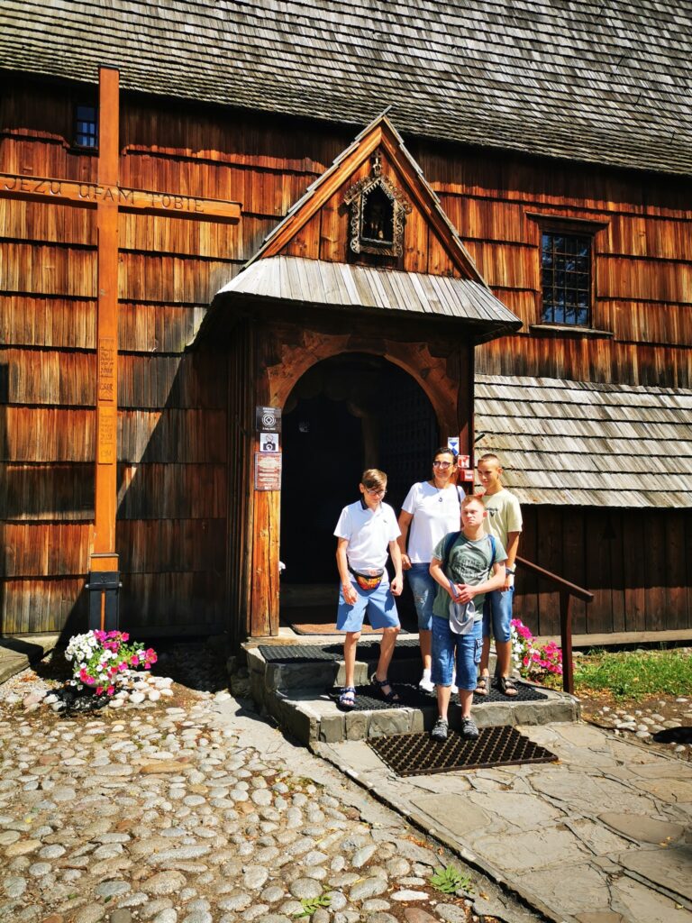 Grupa osób przed wejściem do drewnianego kościoła