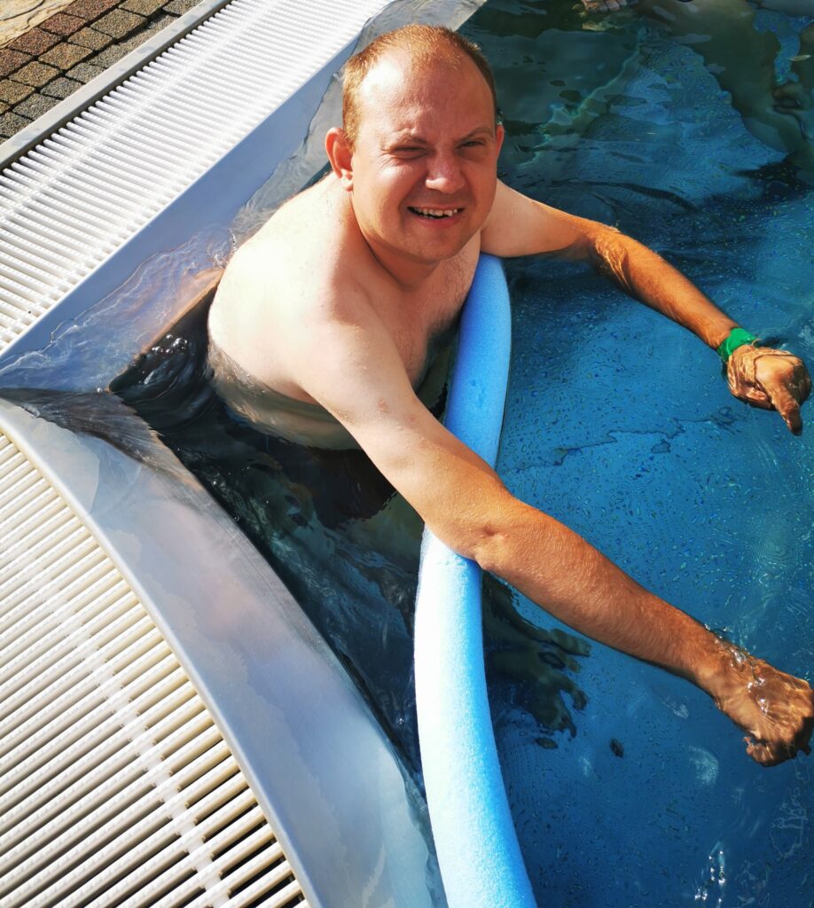 Mężczyzna w basenie. Pod rękami trzyma sprzęt do nauki pływania - tzw. makaron. 