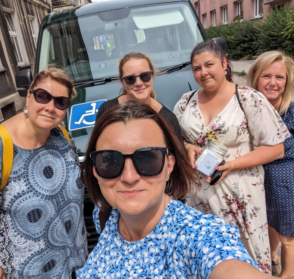 Zdjęcie typu selfie pięciu kobiet. W tle zielony bus., 