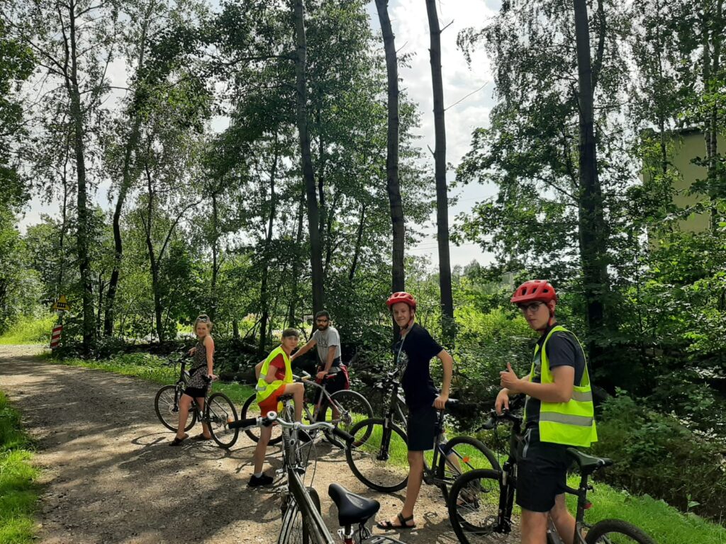 Grupa osób stojących z rowerami na leśnej ścieżce. 