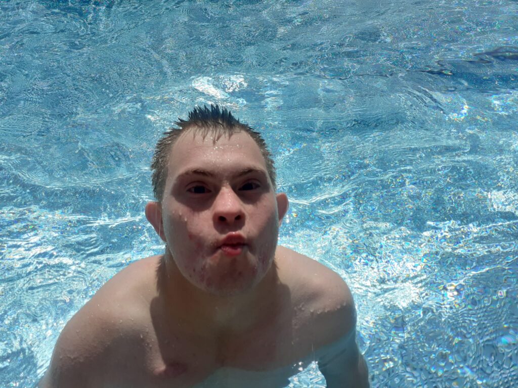 Chłopiec w basenie robiący śmieszną minę do zdjęcia. 