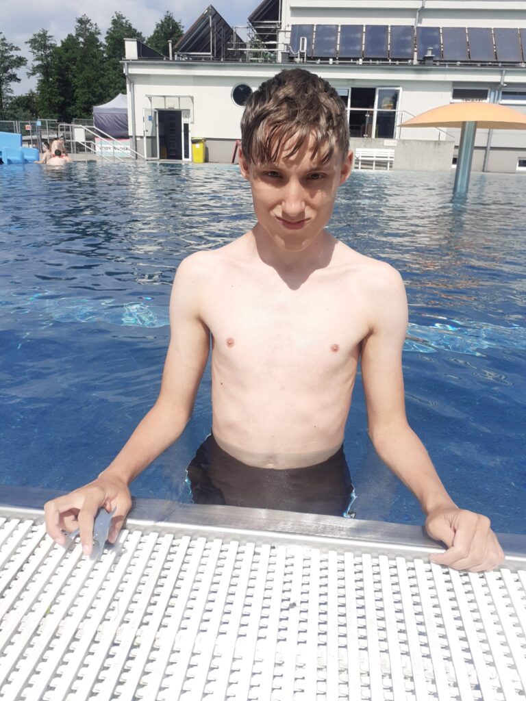 chłopiec stojący w wodzie przy brzegu basenu. 